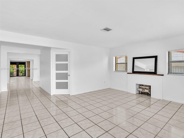 tiled spare room featuring a fireplace, french doors, and a healthy amount of sunlight