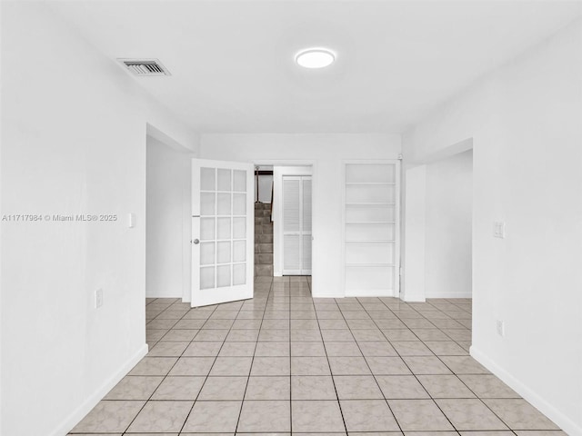 tiled empty room featuring built in shelves and french doors