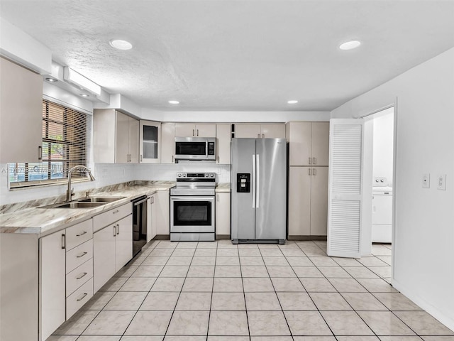 kitchen with sink, backsplash, washer / dryer, light tile patterned floors, and appliances with stainless steel finishes