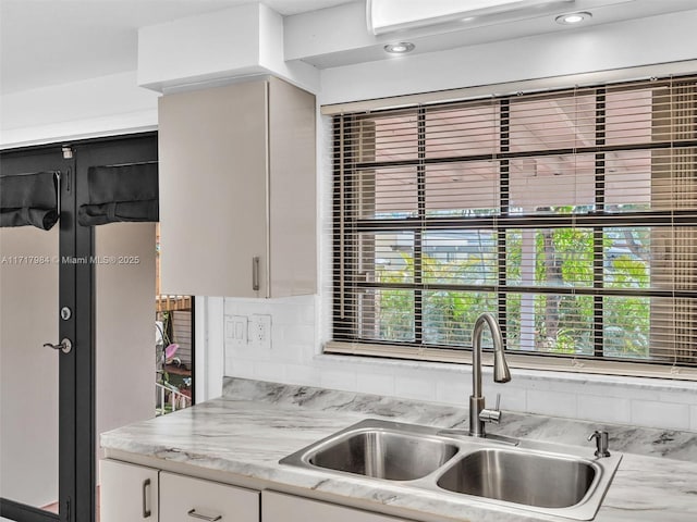 kitchen featuring tasteful backsplash, light stone countertops, sink, and white cabinets