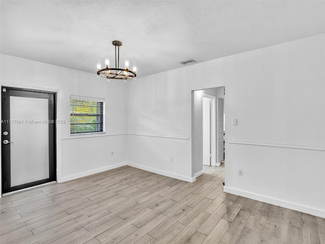 empty room with light wood-type flooring and a notable chandelier