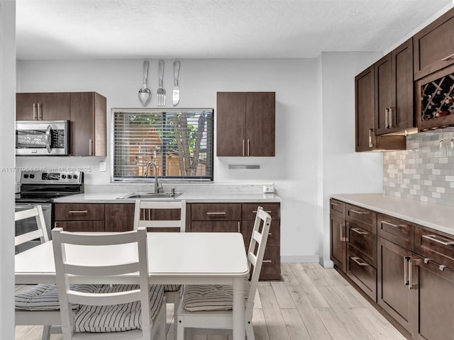 kitchen with backsplash, a textured ceiling, stainless steel appliances, sink, and light hardwood / wood-style flooring