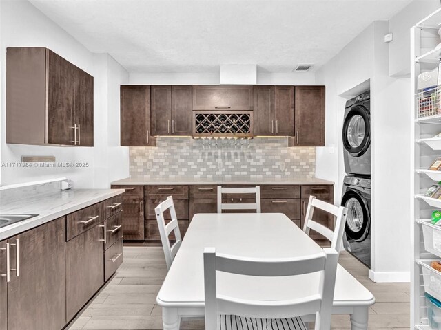 kitchen with decorative backsplash, dark brown cabinetry, and stacked washing maching and dryer