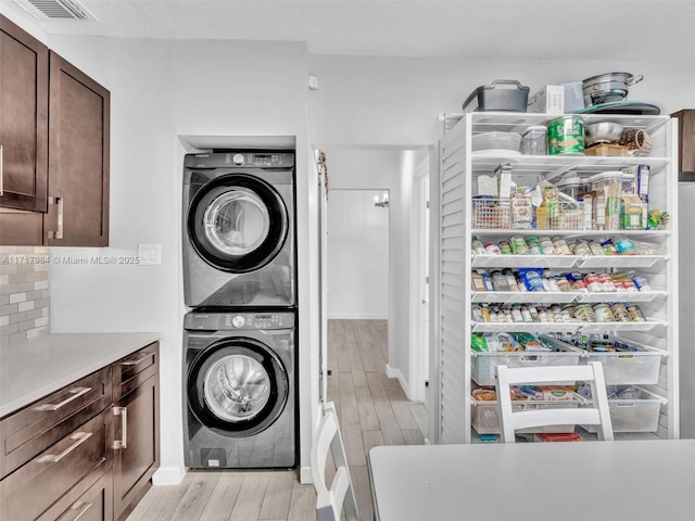 laundry room featuring stacked washing maching and dryer and light hardwood / wood-style floors