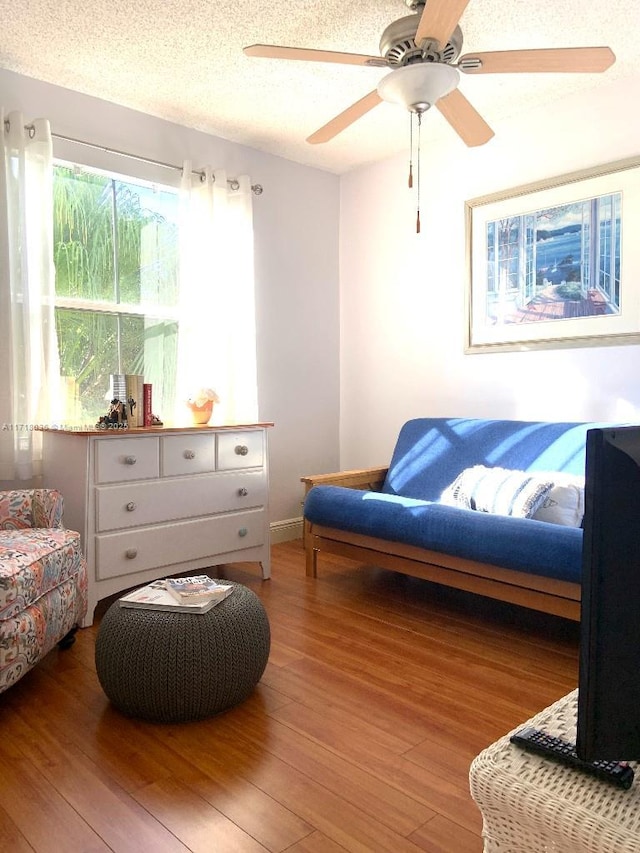 living area with hardwood / wood-style flooring, ceiling fan, and a textured ceiling