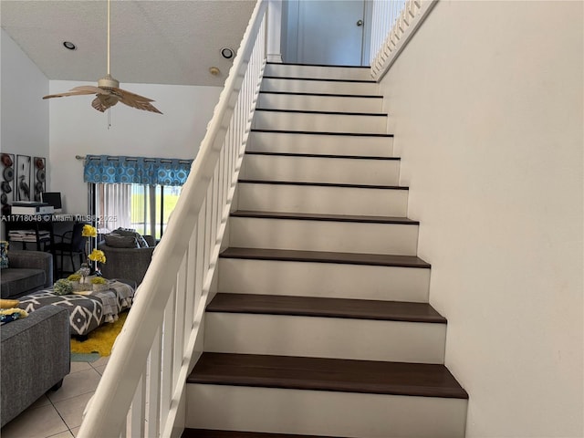 stairs featuring tile patterned flooring, ceiling fan, a towering ceiling, and a textured ceiling