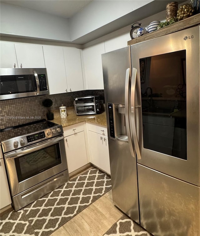 kitchen with light stone countertops, white cabinetry, stainless steel appliances, and light hardwood / wood-style flooring