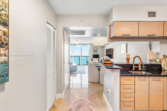 kitchen with light brown cabinets, sink, hanging light fixtures, and dark stone countertops