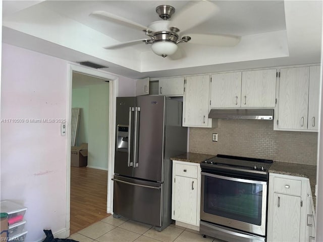 kitchen with dark stone counters, decorative backsplash, light tile patterned floors, a tray ceiling, and stainless steel appliances