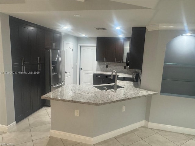 kitchen with sink, stainless steel refrigerator with ice dispenser, light stone countertops, light tile patterned floors, and kitchen peninsula