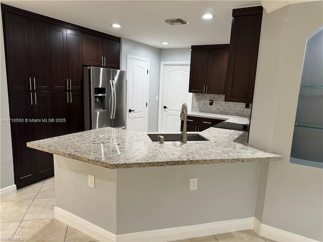 kitchen with sink, stainless steel refrigerator with ice dispenser, light tile patterned floors, light stone counters, and kitchen peninsula