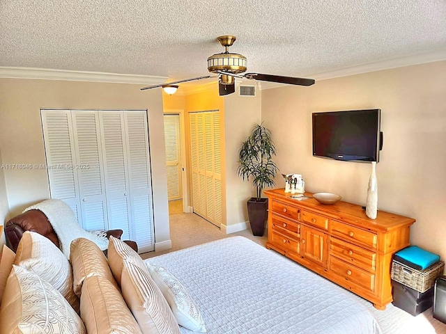 bedroom with a textured ceiling, ceiling fan, crown molding, and two closets