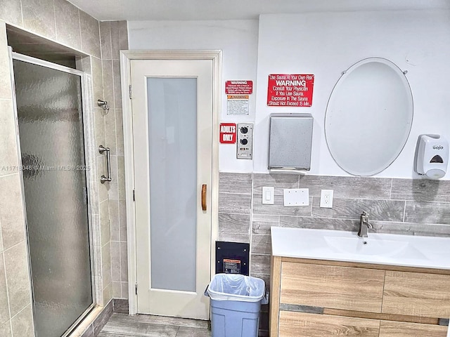 bathroom featuring vanity, a shower with shower door, tile walls, and tasteful backsplash