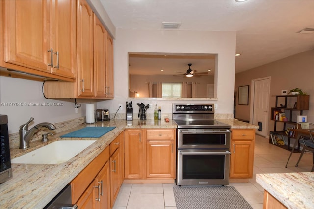 kitchen with ceiling fan, sink, light stone counters, range with two ovens, and light tile patterned flooring