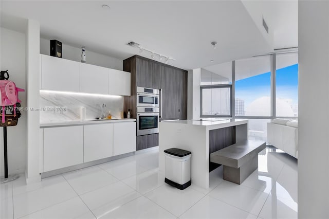 kitchen featuring a center island, white cabinets, light tile patterned floors, dark brown cabinets, and a wall of windows