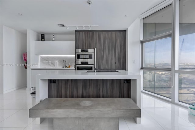 kitchen with light countertops, double oven, light tile patterned flooring, a sink, and modern cabinets