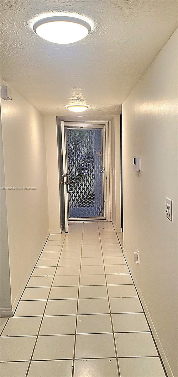 hall featuring light tile patterned floors, baseboards, and a textured ceiling