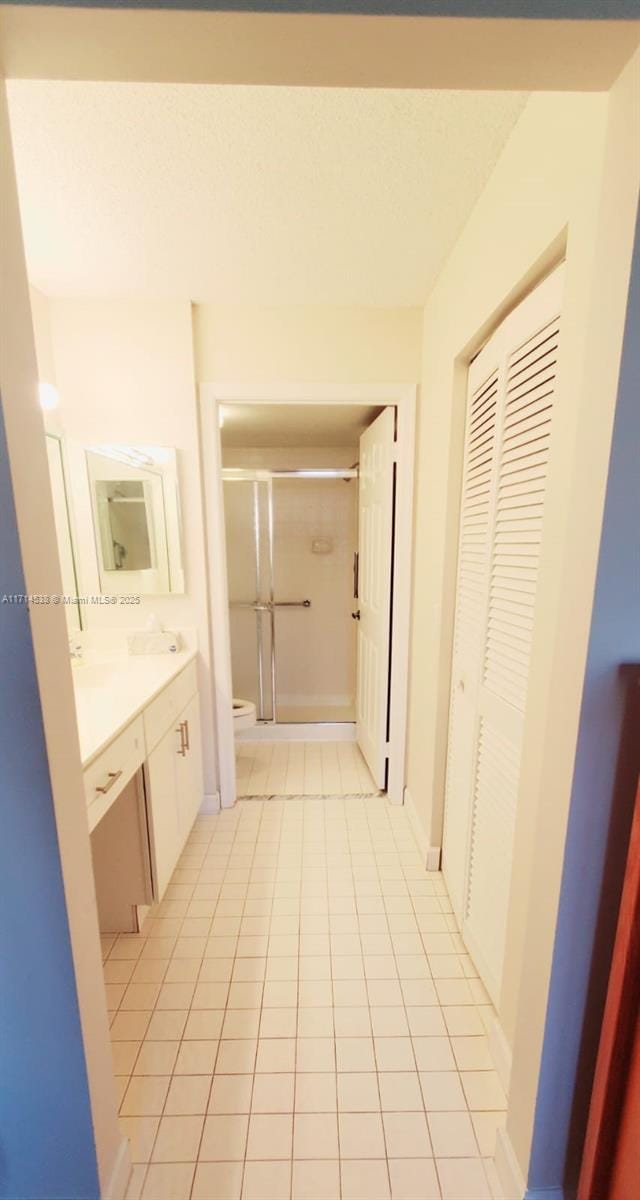 bathroom featuring tile patterned floors, toilet, a shower with door, and vanity