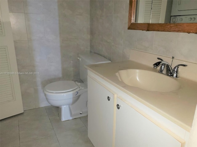 bathroom featuring vanity, tile patterned flooring, toilet, tile walls, and stacked washer / dryer