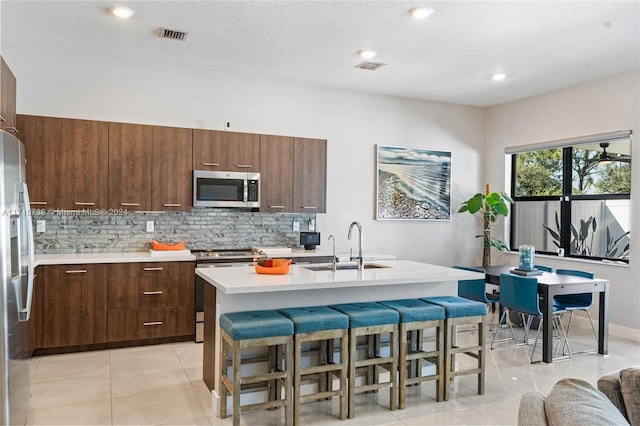 kitchen featuring sink, light tile patterned floors, an island with sink, appliances with stainless steel finishes, and a breakfast bar area