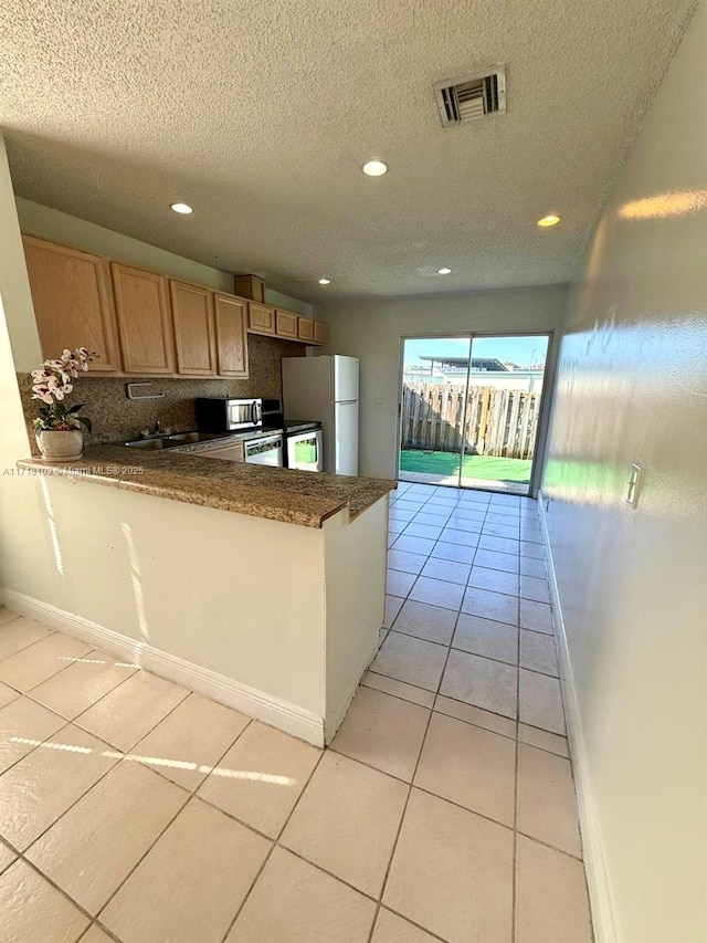 kitchen with decorative backsplash, white refrigerator, light tile patterned flooring, and kitchen peninsula