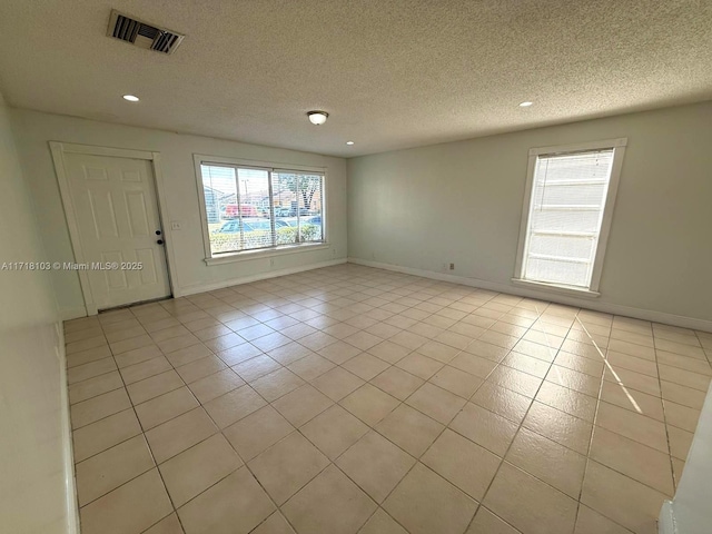 tiled empty room featuring a textured ceiling and a healthy amount of sunlight