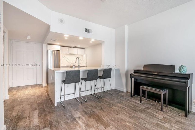 kitchen with dark wood-style flooring, a breakfast bar, visible vents, white cabinets, and a peninsula