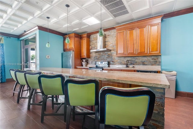 kitchen featuring a kitchen bar, stainless steel appliances, hanging light fixtures, wall chimney exhaust hood, and sink