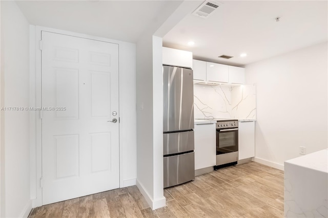 kitchen featuring backsplash, electric stove, light wood-type flooring, stainless steel refrigerator, and white cabinets