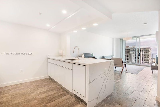 kitchen with floor to ceiling windows, kitchen peninsula, hanging light fixtures, white cabinets, and sink