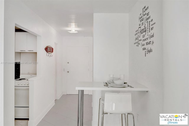 interior space with a kitchen bar, light tile patterned floors, white range, and white cabinetry