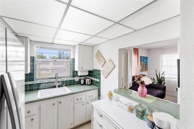 kitchen with stainless steel fridge, tasteful backsplash, a drop ceiling, sink, and white cabinets