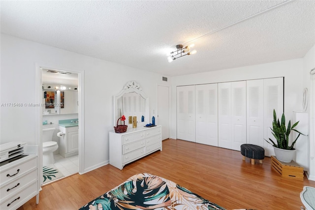 bedroom with ensuite bathroom, sink, a textured ceiling, light hardwood / wood-style floors, and a closet