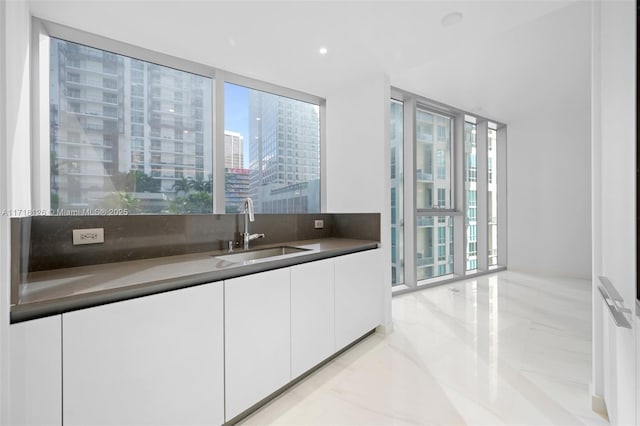 bar featuring floor to ceiling windows, white cabinetry, sink, and tasteful backsplash