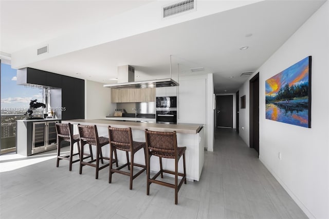 kitchen featuring a kitchen breakfast bar, a kitchen island, built in microwave, oven, and wine cooler