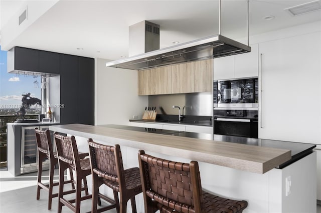 kitchen with sink, wall chimney exhaust hood, built in microwave, wall oven, and a breakfast bar area