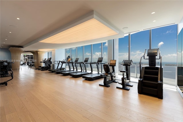 gym featuring expansive windows, a water view, a healthy amount of sunlight, and light wood-type flooring