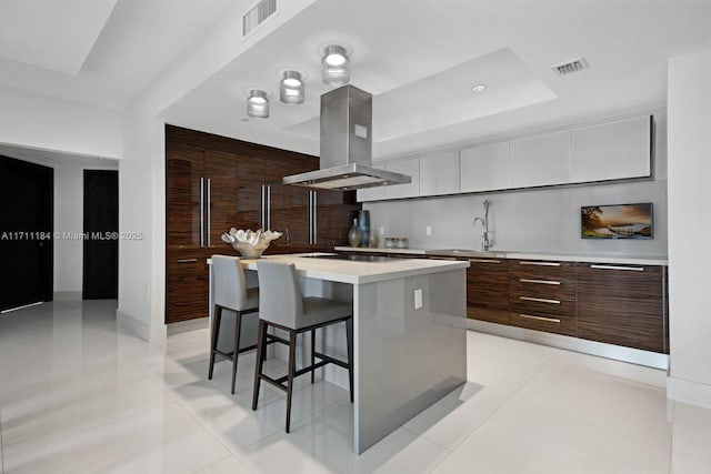 kitchen featuring white cabinetry, a center island, a raised ceiling, island exhaust hood, and light tile patterned floors