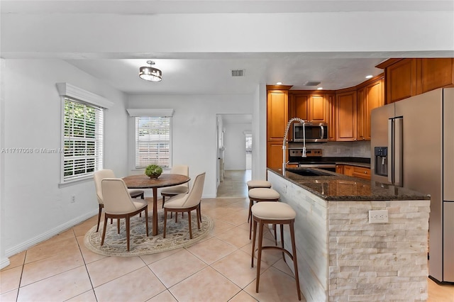 kitchen featuring dark stone counters, decorative backsplash, appliances with stainless steel finishes, light tile patterned flooring, and a kitchen bar