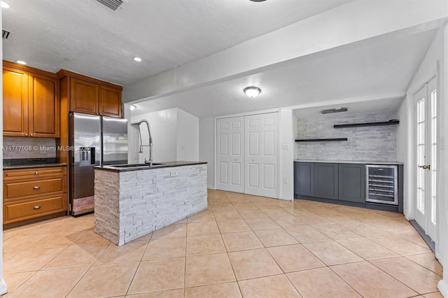 kitchen featuring stainless steel fridge, light tile patterned floors, an island with sink, and wine cooler