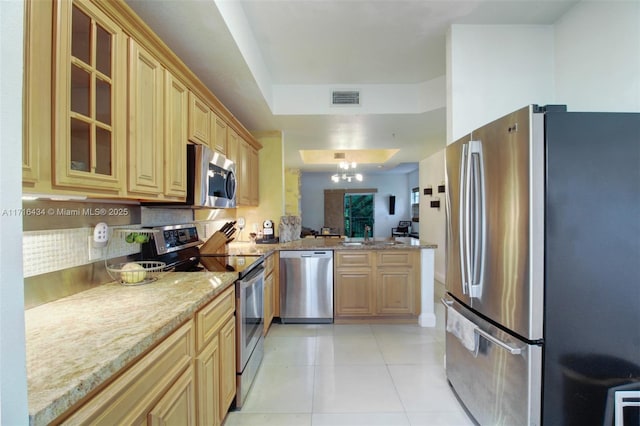 kitchen featuring light stone countertops, stainless steel appliances, a notable chandelier, light brown cabinetry, and light tile patterned flooring