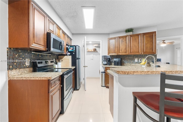 kitchen with kitchen peninsula, appliances with stainless steel finishes, a breakfast bar, a textured ceiling, and ceiling fan