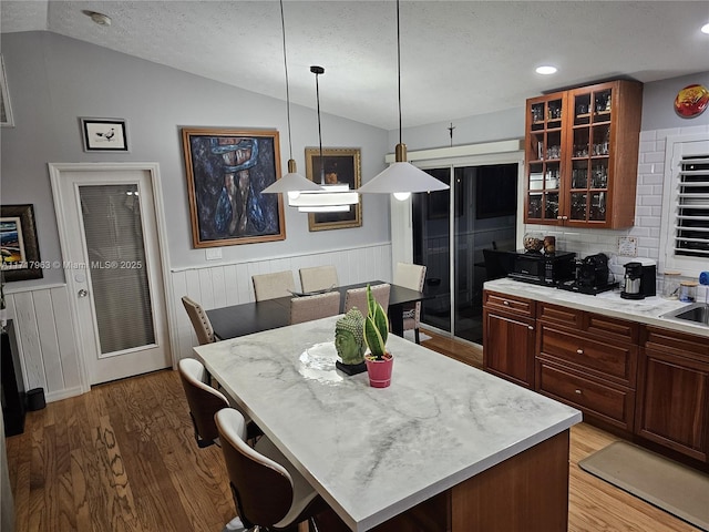 kitchen featuring light hardwood / wood-style flooring, a kitchen island, decorative light fixtures, and vaulted ceiling