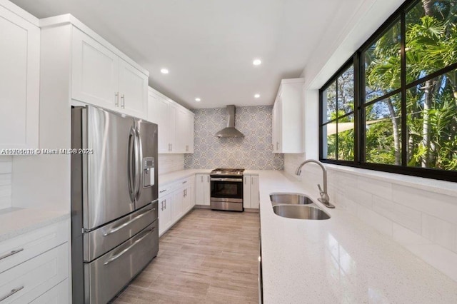 kitchen with appliances with stainless steel finishes, white cabinetry, sink, light stone countertops, and wall chimney range hood