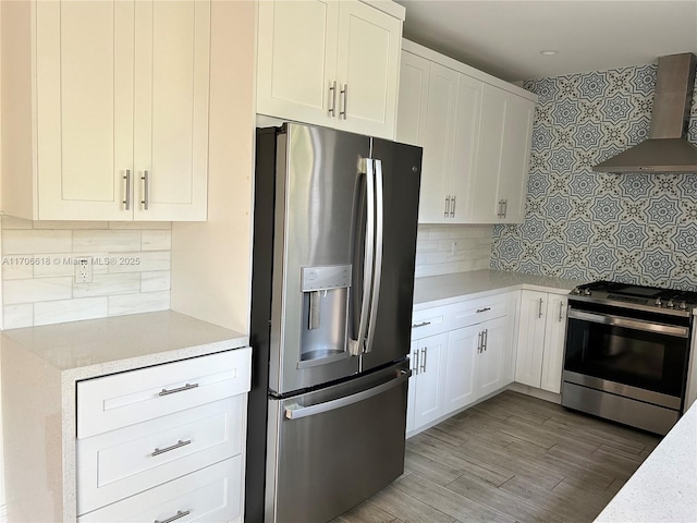 kitchen featuring white cabinets, stainless steel appliances, decorative backsplash, and wall chimney range hood