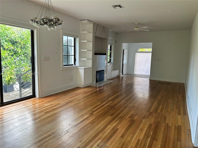 unfurnished living room with hardwood / wood-style flooring, a tiled fireplace, and ceiling fan with notable chandelier