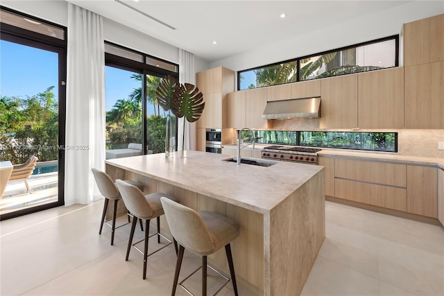 kitchen with a breakfast bar, extractor fan, sink, light brown cabinets, and a center island with sink