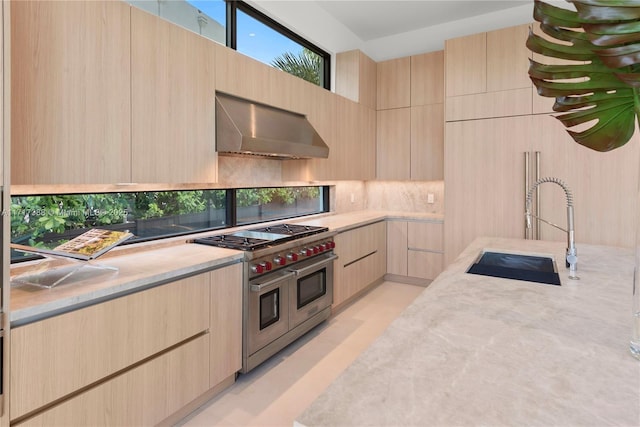 kitchen featuring range with two ovens, wall chimney range hood, sink, and light brown cabinetry