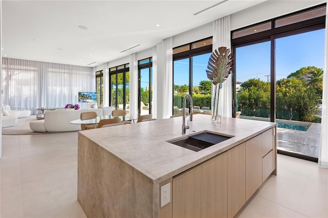 kitchen with a kitchen island with sink, sink, light tile patterned floors, and light brown cabinets