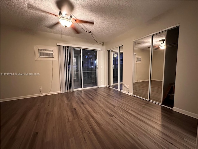 unfurnished room with an AC wall unit, ceiling fan, dark wood-type flooring, and a textured ceiling